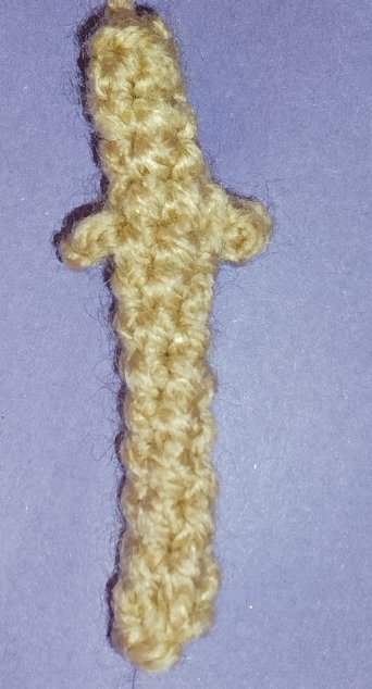 A close-up of the crocheted sword in a beige color, showing the handle with the picot stitches forming a small guard, and the beginning of the blade.