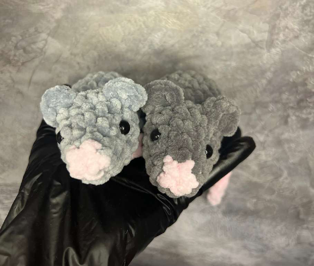 Two crocheted mice, a light grey one and a dark grey one, both with pink noses, showcasing different ear sizes.