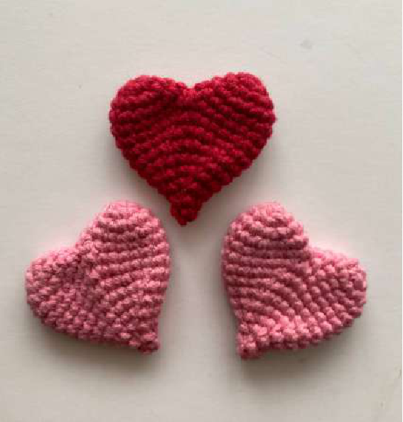 Three crocheted hearts in pink and red shades