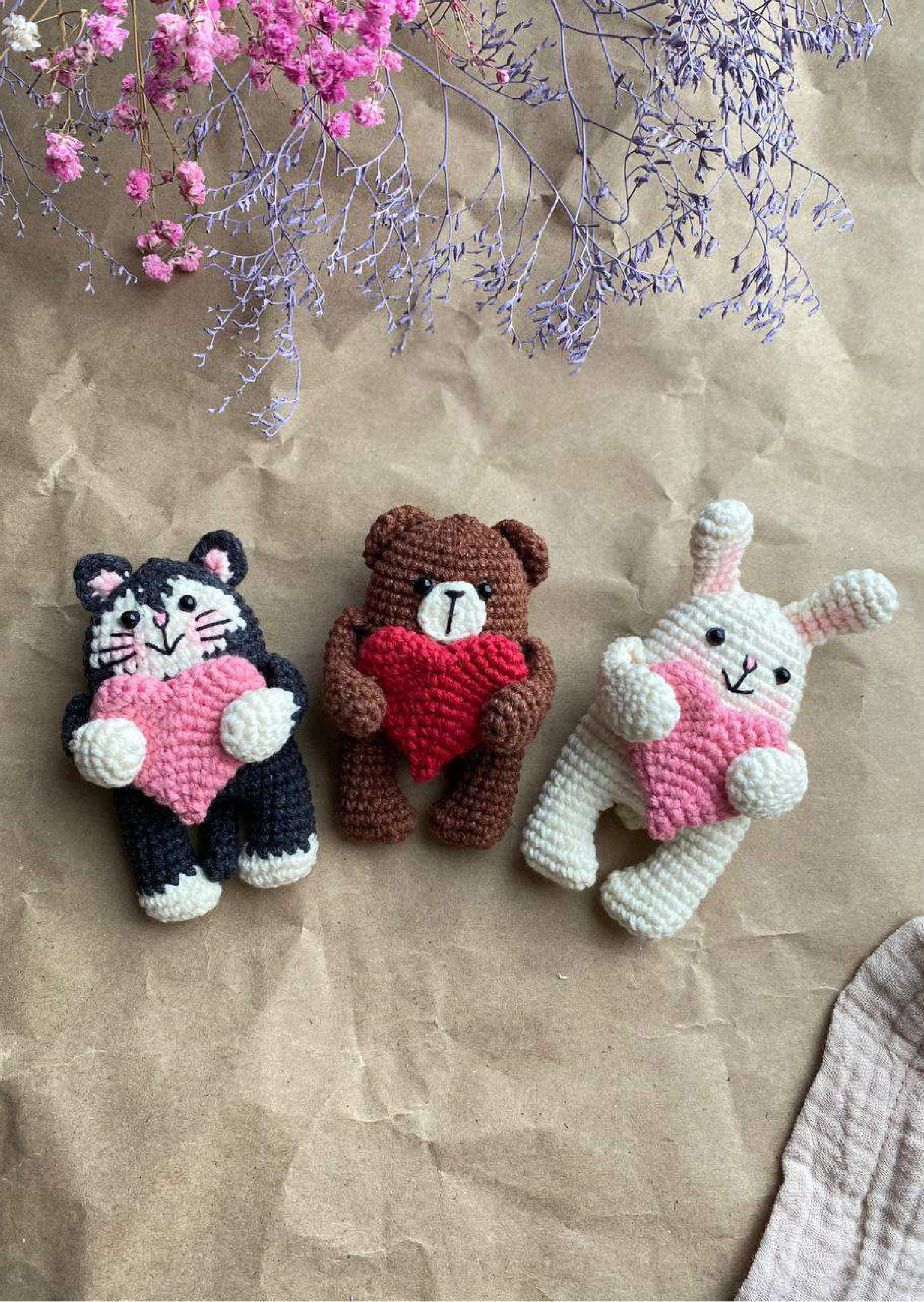 Three finished crocheted animal magnets displayed with dried flowers on craft paper